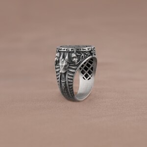 May include: A silver ring with an intricate design featuring an Egyptian god's head and hieroglyphics.