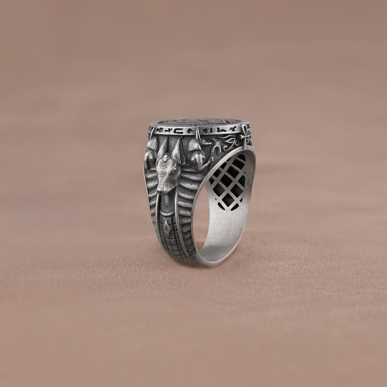 May include: A silver ring with an intricate design featuring an Egyptian god's head and hieroglyphics.