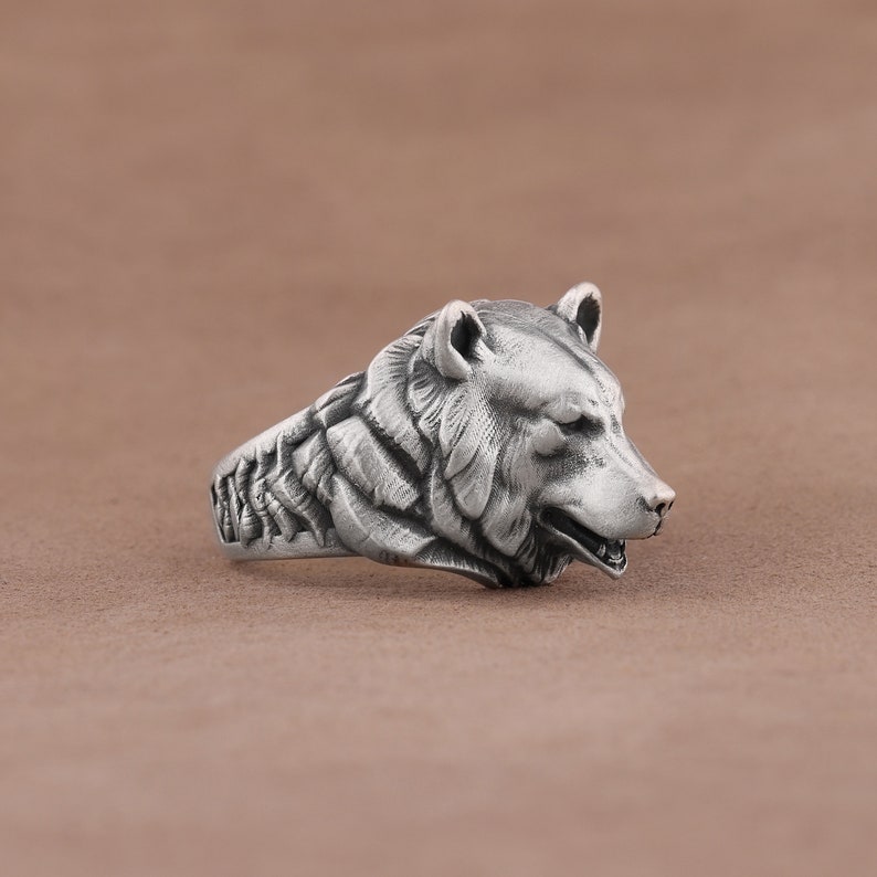 May include: A silver ring with a detailed bear head design. The bear's head is facing to the right and has a textured surface.