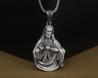 May include: Silver pendant necklace featuring a detailed depiction of Jesus Christ with his heart exposed, surrounded by rays of light. The necklace has a silver chain.