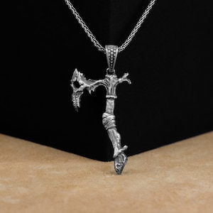 以下が含まれることがあります： 精巧で複雑なデザインの銀製の斧のペンダントネックレス。斧は鋭い刃と質感のある柄を持っています。