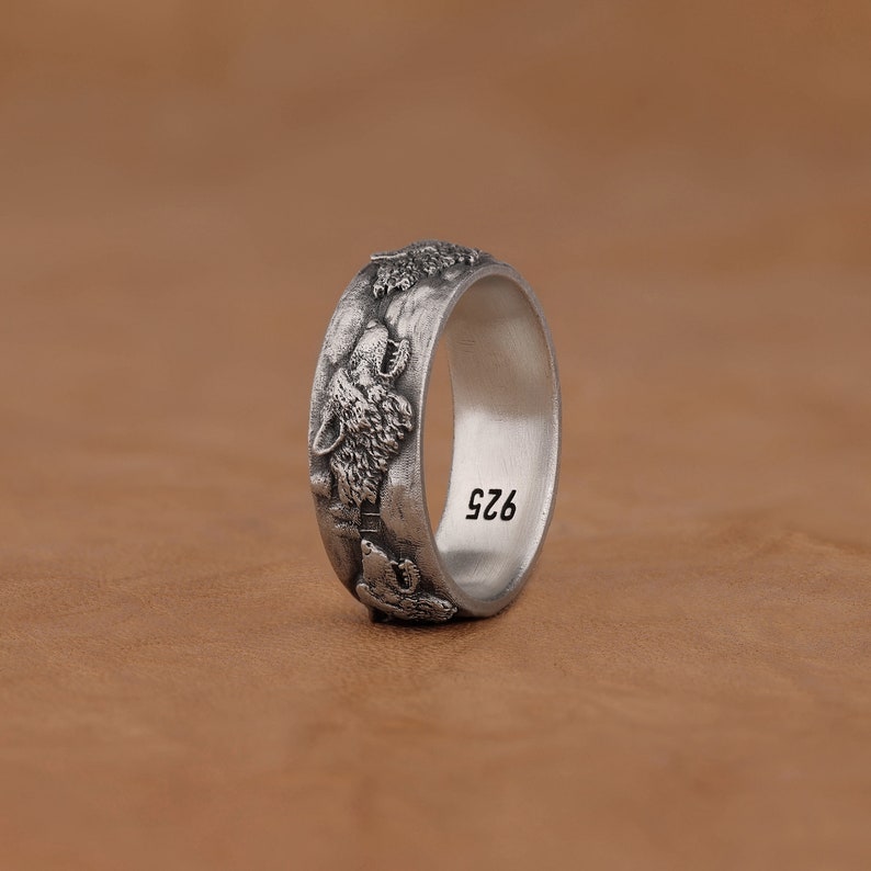 May include: A silver ring with a design of wolf heads around the band. The inside of the band is engraved with the number "925".