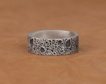 May include: A silver ring with a textured surface that resembles the moon's surface.