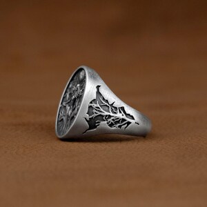 May include: A silver ring featuring an intricate design of a tree with roots and branches. The ring is crafted from metal and has a polished finish.