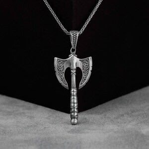 May include: A silver axe pendant with intricate Celtic knotwork designs on the blade and handle. The pendant is hanging from a silver chain.