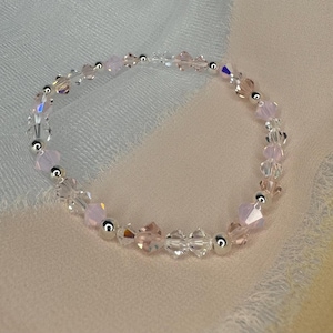 以下が含まれることがあります： クリアとピンクのクリスタルビーズが交互に並んだ、繊細なブレスレット。シルバーのアクセントが施されています。