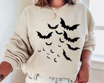 Könnte beinhalten: Ein sandfarbener Pullover mit einem schwarzen Fledermaus-Design. Die Fledermäuse sind in verschiedenen Größen und über die Vorderseite des Pullovers verteilt.