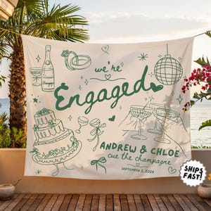 May include: A white fabric banner featuring dark green line art illustrations of a wedding cake, champagne bottle, disco ball, and rings. The text reads "we're Engaged", "ANDREW & CHLOE", "cue the champagne", and "SEPTEMBER 2, 2026" in a mix of fonts.
