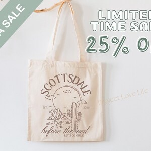 May include: Beige tote bag with a Scottsdale, Arizona design. The design includes a desert landscape with a cactus, mountains, and the text "Scottsdale" and "before the veil". The bag also has the text "MEGA SALE" and "LIMITED TIME SALE 25% OFF".
