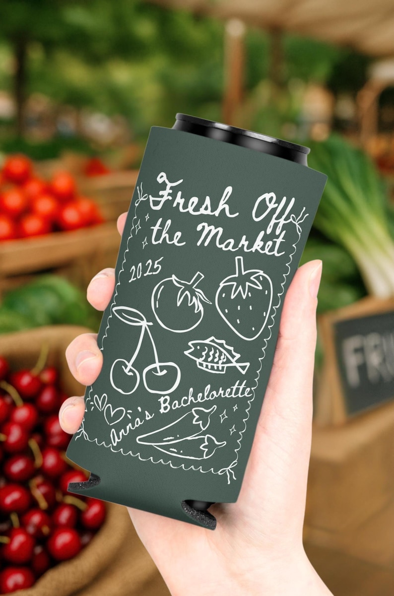 May include: Dark green can cooler with white text and illustrations. The text reads "Fresh Off the Market 2025" with drawings of a cherry, tomato, strawberry, fish, and pepper. The text "Anna's Bachelorette" is also visible.
