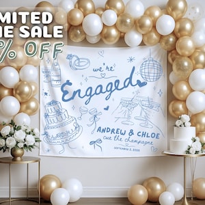 May include: A white fabric backdrop featuring blue line art of a wedding cake, champagne, rings, and a disco ball, with the text "we're Engaged", "ANDREW & CHLOE", "cue the champagne", and "SEPTEMBER 2, 2026". It is framed by a gold and white balloon arch.