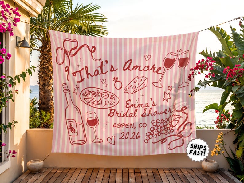 May include: A pink and white striped banner with the words "That's Amore" and "Emma's Bridal Shower Aspen, CO 2026" in red. The banner features illustrations of wine, food, and celebratory elements.