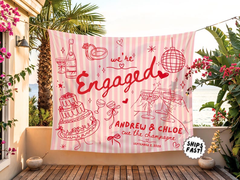 May include: A rectangular fabric banner with vertical light pink and white stripes featuring red line art illustrations of a champagne bottle, wedding rings, a disco ball, a tiered cake, and cocktail glasses with the text "we're Engaged", "ANDREW & CHLOE", "cue the champagne", and "SEPTEMBER 2, 2026".