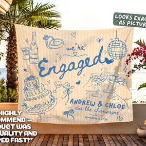 May include: A rectangular fabric banner with a light yellow and white vertical striped pattern. The banner features blue line art illustrations of a champagne bottle, a tiered cake, a disco ball, and cocktail glasses, with the text "we're Engaged", "ANDREW & CHLOE", "cue the champagne", and "SEPTEMBER 2, 2026".