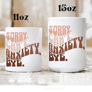 K&ouml;nnte beinhalten: Zwei wei&szlig;e Keramikbecher mit einem braunen, rosa und pfirsichfarbenen Design. Die Becher haben den Text "Sorry Can't Anxiety Bye." Der kleinere Becher ist 11 oz und der gr&ouml;&szlig;ere Becher ist 15 oz.