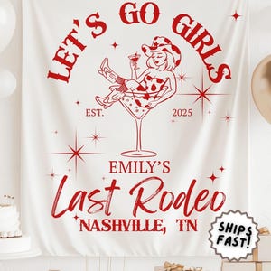 May include: White fabric banner with red text and graphics. The banner reads "LET'S GO GIRLS" and "EMILY'S Last Rodeo NASHVILLE, TN". A cowgirl illustration is in a martini glass. The banner is for a bachelorette party.