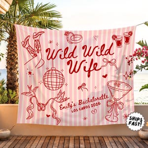 May include: Pink and white striped banner with red illustrations and text. The banner reads "Wild Wild Wife" with additional text "Emily's Bachelorette Los Cabos 2026". Includes images of cowboy boots, a disco ball, and cocktails.