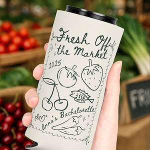 May include: A white can cooler with black trim, featuring the text "Fresh Off the Market" and a series of hand-drawn illustrations including cherries, a tomato, a strawberry, and fish. The text "Anna's Bachelorette" is also included.