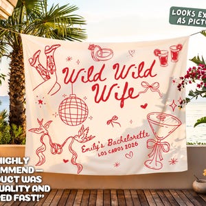 May include: A cream-colored banner with red illustrations and text. The banner reads "Wild Wild Wife" with additional text "Emily's Bachelorette Los Cabos 2026". The design includes images of cowboy boots, a disco ball, and cocktails.