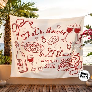 May include: A white banner with red illustrations and text for a bridal shower. The banner features wine glasses, a bottle of wine, cheese, and the words "That's Amore" and "Emma's Bridal Shower, Aspen, CO 2026."