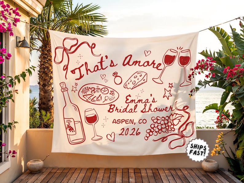 May include: A white banner with red illustrations and text for a bridal shower. The banner features wine glasses, a bottle of wine, cheese, and the words "That's Amore" and "Emma's Bridal Shower, Aspen, CO 2026."