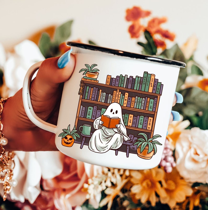 white camp enamel mug with black rim, this ghost mug design has a cottagecore ghost reading a book with bookshelf and coffee mug, perfect gift for book lovers and a great ghost mug for a gothic friend.