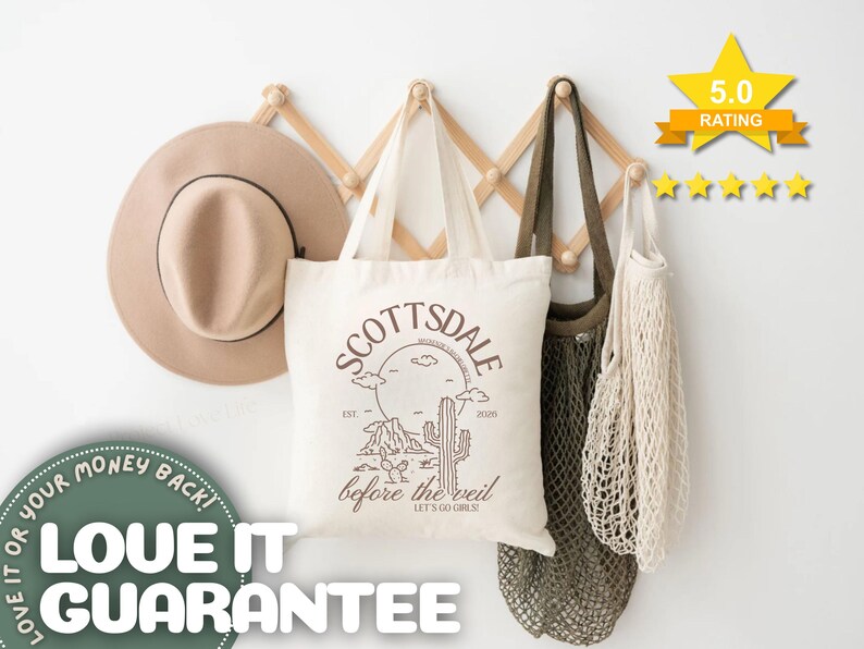 May include: A beige fedora hat, a white tote bag with "SCOTTSDALE before the veil" text, and two mesh bags hang on a wooden rack. The tote bag features a desert landscape design. A 5.0 rating star graphic is visible.