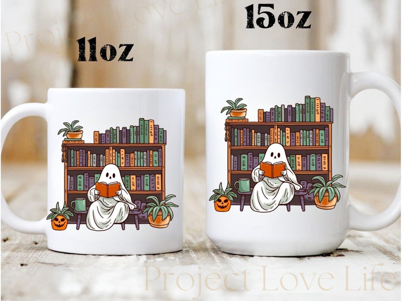 May include: White ceramic mug with a ghost reading a book in front of a bookshelf. The ghost is sitting on a stool with a pumpkin and a plant beside it. The mug has the text "11oz" on the left side and "15oz" on the right side.