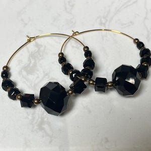 Peut inclure: Paire de créoles dorées ornées de perles noires facettées et de petites perles dorées. Les boucles d'oreilles présentent de grosses perles noires géométriques, créant un look audacieux et élégant. Le design est simple mais saisissant.