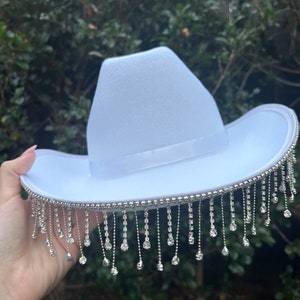May include: A white cowboy hat with a silver rhinestone trim and fringe.