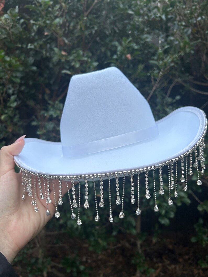 May include: A white cowboy hat with a silver rhinestone trim and fringe.