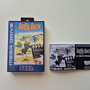 Op de afbeelding: Een Sega Mega Drive videospeldoos en instructiehandleiding voor "Daffy Duck in Hollywood". De doos toont Daffy Duck met een klapbord, met een Hollywood-achtergrond. De handleiding is zwart-wit.