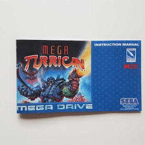 Puede incluir: Un manual de instrucciones de Mega Turrican para Sega Mega Drive. La portada presenta una vibrante ilustración de un guerrero futurista y el título del juego en letras rojas. El manual es azul con los logotipos de Sony y Sega.