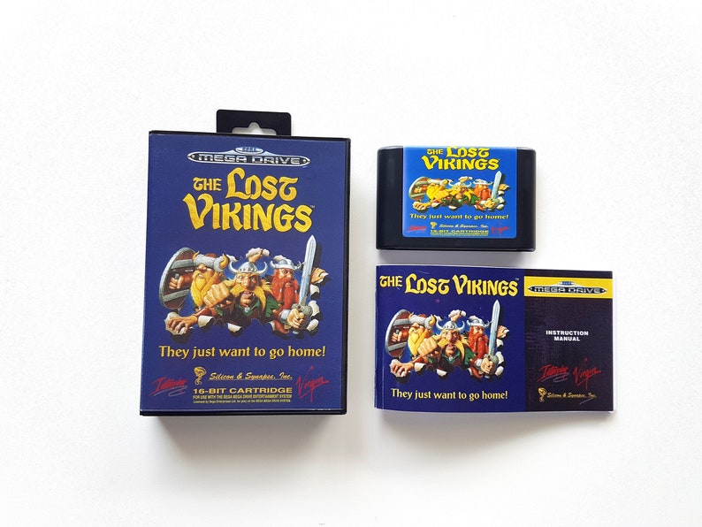 Puede incluir: Un cartucho de juego Sega Mega Drive, un manual de instrucciones y una caja de juego para el juego "The Lost Vikings". La caja del juego es azul con una imagen de tres vikingos. El texto "They just want to go home!" est&aacute; impreso en la caja. El manual de instrucciones tambi&eacute;n es azul con una imagen de los vikingos. El texto "They just want to go home!" est&aacute; impreso en el manual.