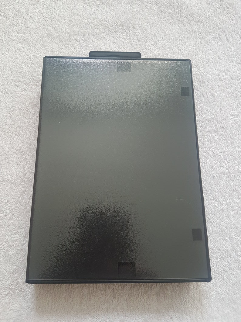 Puede incluir: Una caja de pl&aacute;stico negra con una superficie texturizada. La caja tiene una peque&ntilde;a abertura rectangular en la parte superior e inferior.