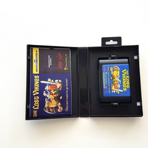 Puede incluir: Una caja de cartucho de juego Sega Genesis negra con un cartucho de juego azul y amarillo en su interior. El cartucho de juego es para el juego "The Lost Vikings". La caja tiene una carcasa de pl&aacute;stico negro con una ventana de pl&aacute;stico transparente para mostrar el cartucho de juego. El cartucho de juego tiene un fondo azul con texto amarillo e im&aacute;genes de los personajes del juego.