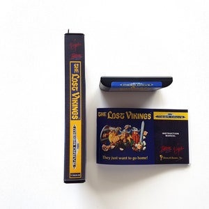 Puede incluir: Un cartucho de juego Sega Mega Drive y un manual de instrucciones para el juego "The Lost Vikings". El cartucho de juego es azul y negro con el texto "Sega Mega Drive" en &eacute;l. El manual de instrucciones es azul y negro con una imagen de los personajes del juego. El texto "The Lost Vikings" est&aacute; impreso en amarillo en el manual. El texto "They just want to go home!" est&aacute; impreso en blanco en el manual.