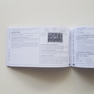 Puede incluir: Un libro abierto en una p&aacute;gina con el t&iacute;tulo "The Lost Vikings" y una descripci&oacute;n de c&oacute;mo jugar al juego. El libro es parte de un juego de mesa.
