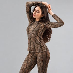 May include: A long-sleeved shirt and matching leggings set featuring a realistic brown and gray tree bark pattern. The garment has a crew neckline and a fitted silhouette, with the textured wood grain print covering the entire surface.
