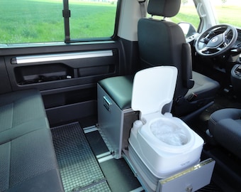 May include: A white portable toilet with a lid open, inside a van. The toilet is in a drawer that is pulled out. The toilet is in a van with black seats and a black floor.