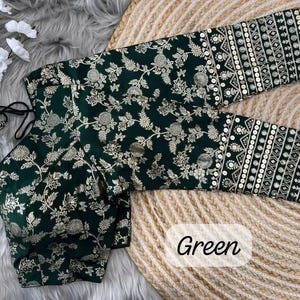 May include: A dark green blouse featuring a gold floral pattern and three-quarter length sleeves with intricate gold embroidery and sequin detailing. The garment includes a tie-back closure with matching tassels and the word Green printed on it.