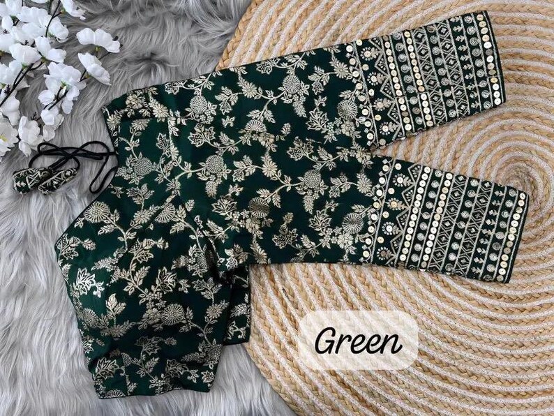 May include: A dark green blouse featuring a gold floral pattern and three-quarter length sleeves with intricate gold embroidery and sequin detailing. The garment includes a tie-back closure with matching tassels and the word Green printed on it.