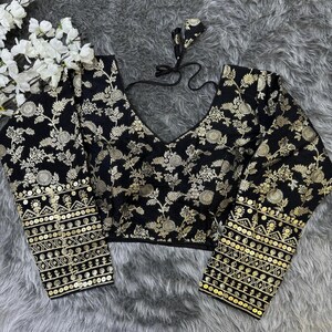 May include: A black long-sleeved blouse featuring an intricate gold floral pattern throughout. The garment has a deep V-neckline with black tie-up strings at the back and cuffs adorned with horizontal bands of gold sequins and geometric embroidery.