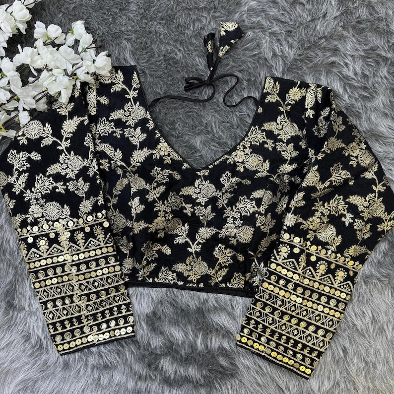 May include: A black long-sleeved blouse featuring an intricate gold floral pattern throughout. The garment has a deep V-neckline with black tie-up strings at the back and cuffs adorned with horizontal bands of gold sequins and geometric embroidery.