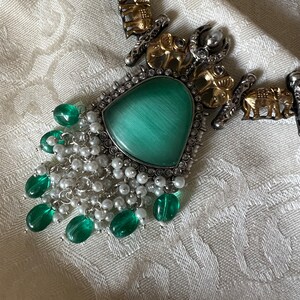 Op de afbeelding: Een zilveren en gouden ketting met een groene stenen hanger en een franje van groene en witte kralen.