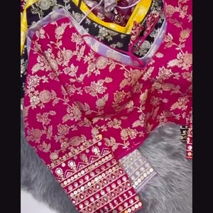 May include: A collection of long-sleeved blouses featuring intricate gold floral embroidery on vibrant fabrics including magenta, black, and yellow. Each blouse has a round neckline and detailed cuffs with geometric patterns and small circular accents.