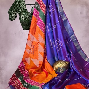 May include: A vibrant sari featuring a bright orange section with white geometric patterns, a deep purple section with thin silver grid lines, and a green border with pink stripes. A dark green blouse with gold polka dots hangs above.