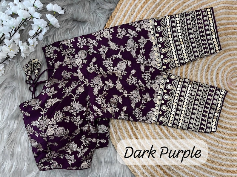 May include: A dark purple blouse featuring intricate silver floral embroidery across the body and sleeves. The cuffs are detailed with horizontal bands of geometric patterns and sequins. The garment includes thin tie-up strings at the neckline.
