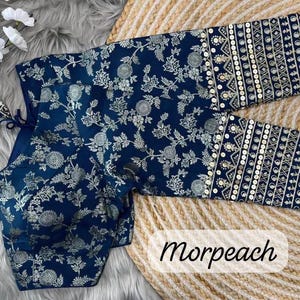 May include: A navy blue blouse featuring a silver floral pattern and long sleeves with decorative bands of geometric embroidery and sequins. The garment includes a tie closure at the back with matching fabric tassels and the text Morpeach.