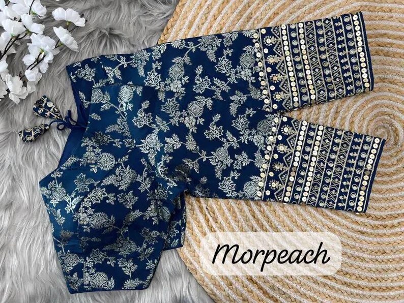 May include: A navy blue blouse featuring a silver floral pattern and long sleeves with decorative bands of geometric embroidery and sequins. The garment includes a tie closure at the back with matching fabric tassels and the text Morpeach.